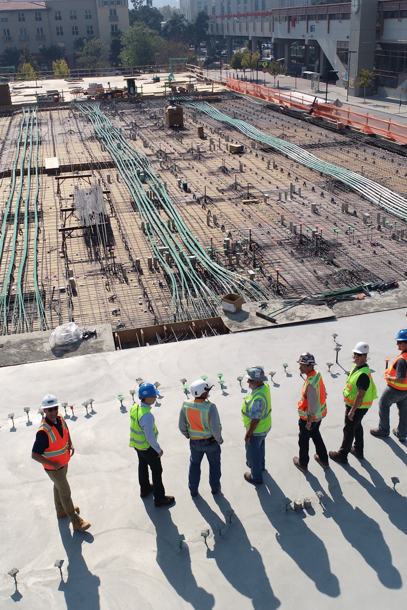 Construction site workers in safety vests on a rebar slab, photo timestamped with SnapProof
