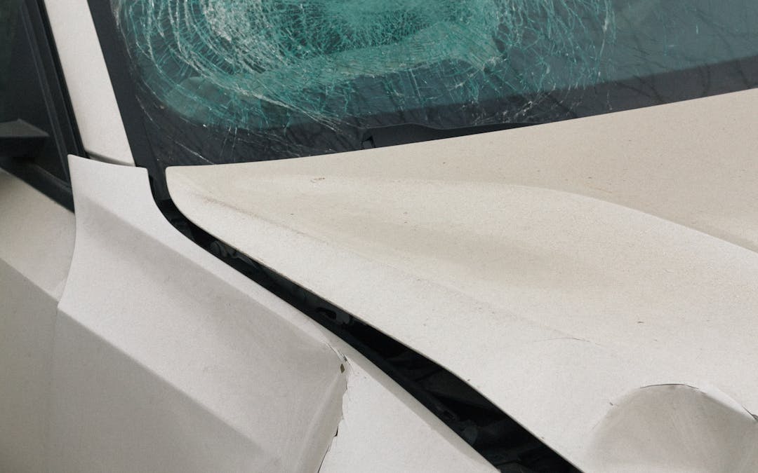 Close-up of a car with shattered windshield and front-end accident damage, scene documented with GPS-stamped photo